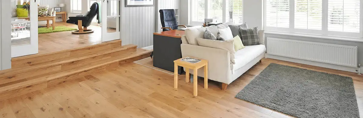 A modern living room with professionally installed laminate flooring, a beige sofa, a small side table, a gray rug, and large windows with white shutters in Fort Collins, CO